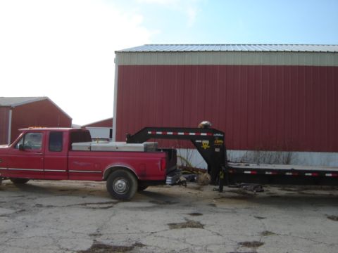 1992 Ford Bronco - A red pickup truck is parked next to a large red barn, attached to a gooseneck trailer.