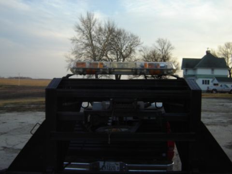 1992 Ford Bronco - The rear of a tow truck bed is shown with a light bar on top, with a house and another vehicle in the background.