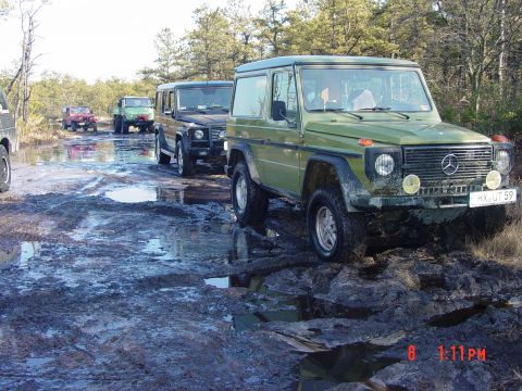 1995 Dodge 1500 - Several off-road vehicles navigate a wet, muddy path through a wooded area.