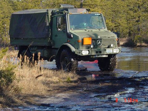 1995 Dodge 1500 - This military truck navigates a wet, off-road environment with tall grass and trees in the background.