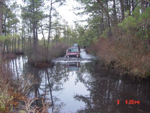 1995 Dodge 1500 - Two SUVs navigate a water and mud obstacle on a wooded trail.