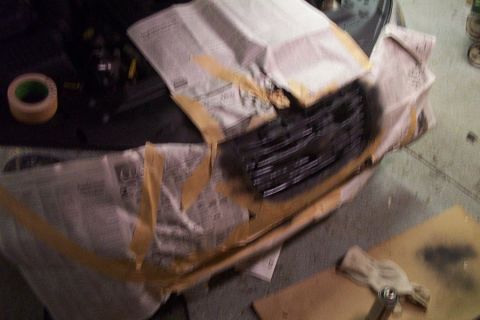 1999 Chrysler 300M - A car grille is being prepped for painting, covered in protective materials.