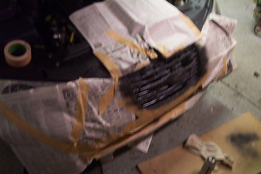 Car front masked with newspaper and tape while the grille is spray-painted black