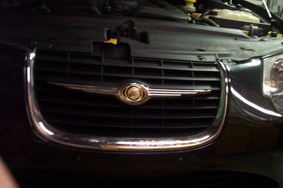 Black Chrysler sedan front grille with chrome surround and winged badge, hood open