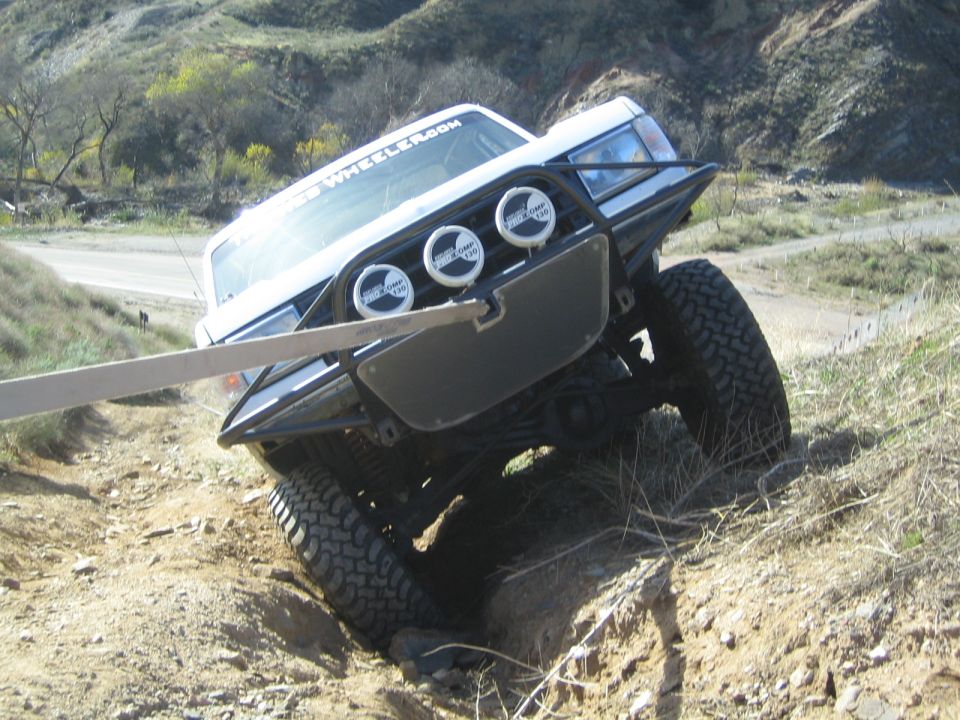 Front view of white lifted truck with brush guard and three off-road lights climbing rocky terrain