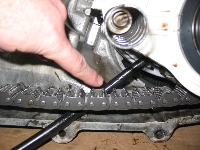 Hand and pry bar over a metal drive chain inside an aluminum housing