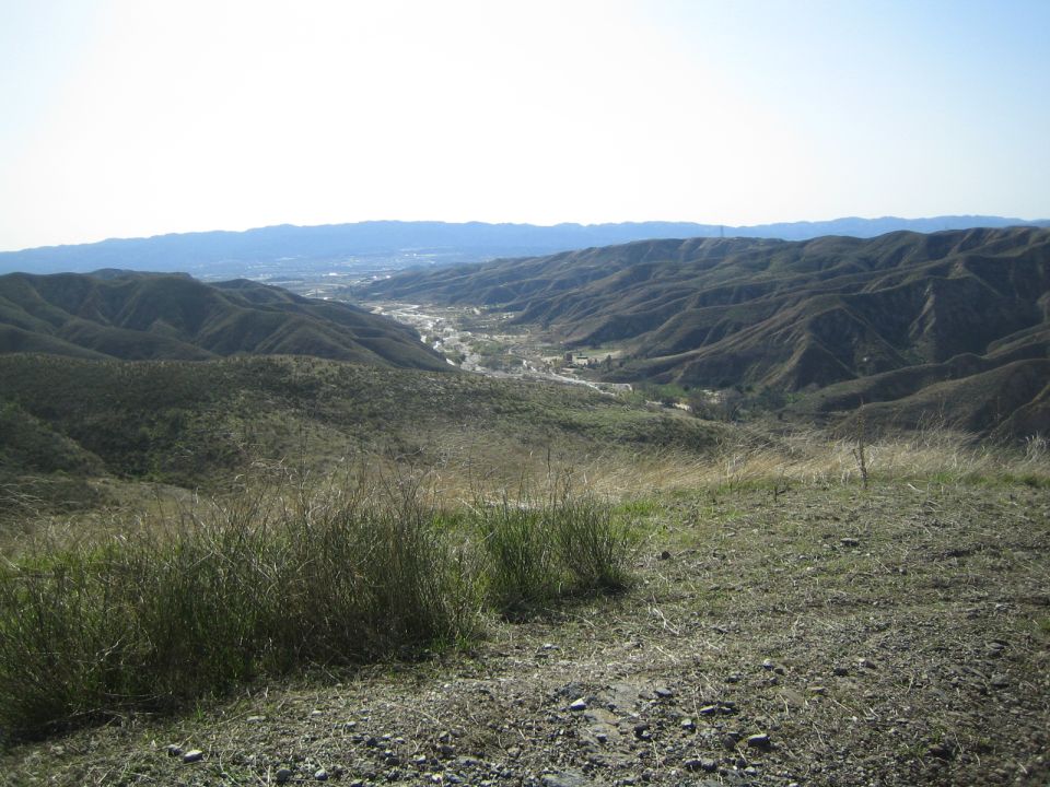 Scenic overlook of a valley town between rolling brown hills under hazy sky