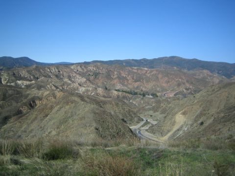 1990 Ford Bronco - rugged landscape of eroded multicolored hills with a paved road winding through the valley under a clear blue sky.