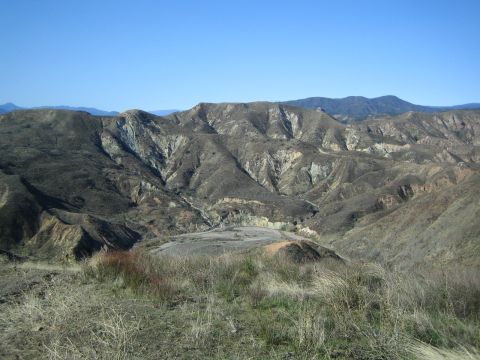1990 Ford Bronco - view across deeply eroded mountain ridges and dry golden brush toward distant peaks under a clear blue sky.