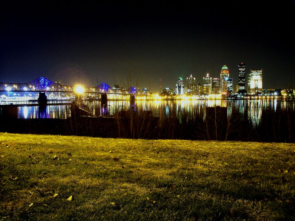 city skyline across a river at night, with a bridge and reflections in the water