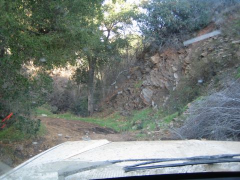 1990 Ford Bronco - Through a windshield over a white hood, a narrow dirt trail winds beside a rocky hillside among oak trees.