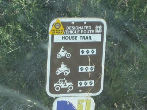 1990 Ford Bronco - Close-up of a brown forest service sign for House Trail showing motorcycle, ATV and 4x4 difficulty diamonds against green foliage.