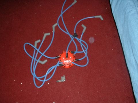 1985 Ford Bronco - MSD distributor cap and spark plug wires are laid out on a red carpet next to a small bracket.