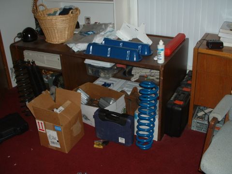 1985 Ford Bronco - Various engine parts, including blue valve covers and coil springs, are organized on a desk and scattered on the floor.