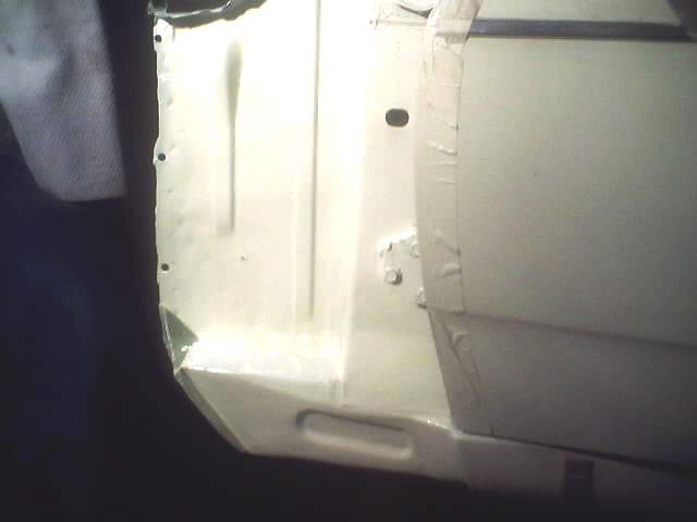 Close-up of a car's interior door panel, showing primer and some tape