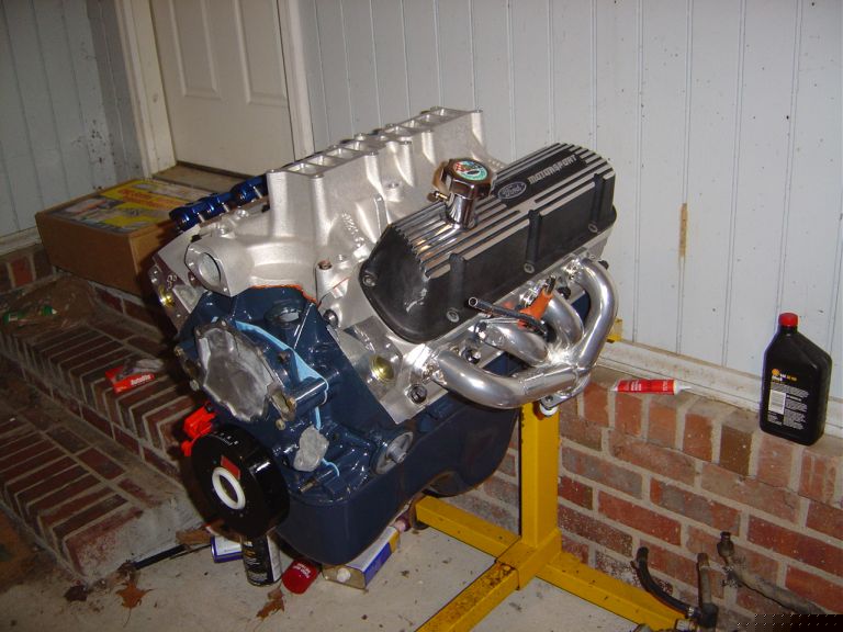 Built Ford V8 with blue block, Motorsport valve covers, and chrome headers on an engine stand
