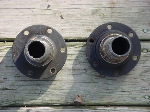 1983 Ford Bronco - Two metal wheel hubs with bolt holes and splined centers are displayed on a weathered wooden surface.