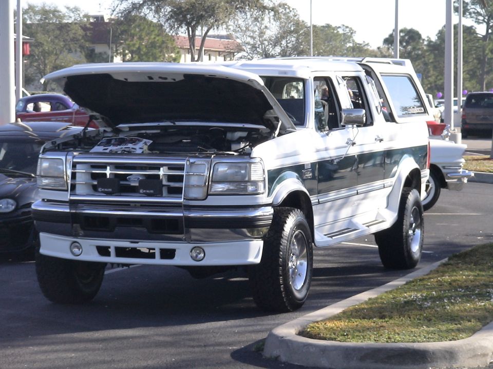 White and green lifted full-size SUV with hood up and chrome grille guard in a parking lot