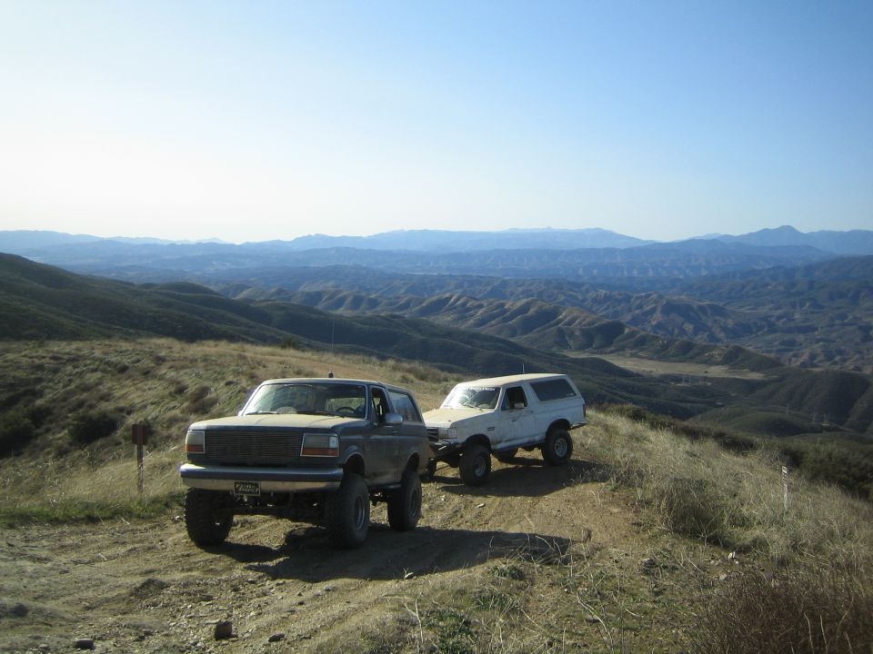 Two lifted Ford SUVs parked on a dirt ridge overlooking distant hills