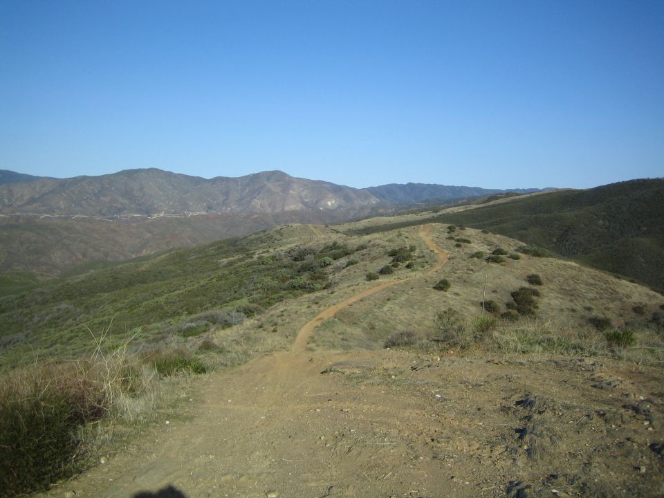Dirt trail winding along a ridge toward distant mountains under blue sky