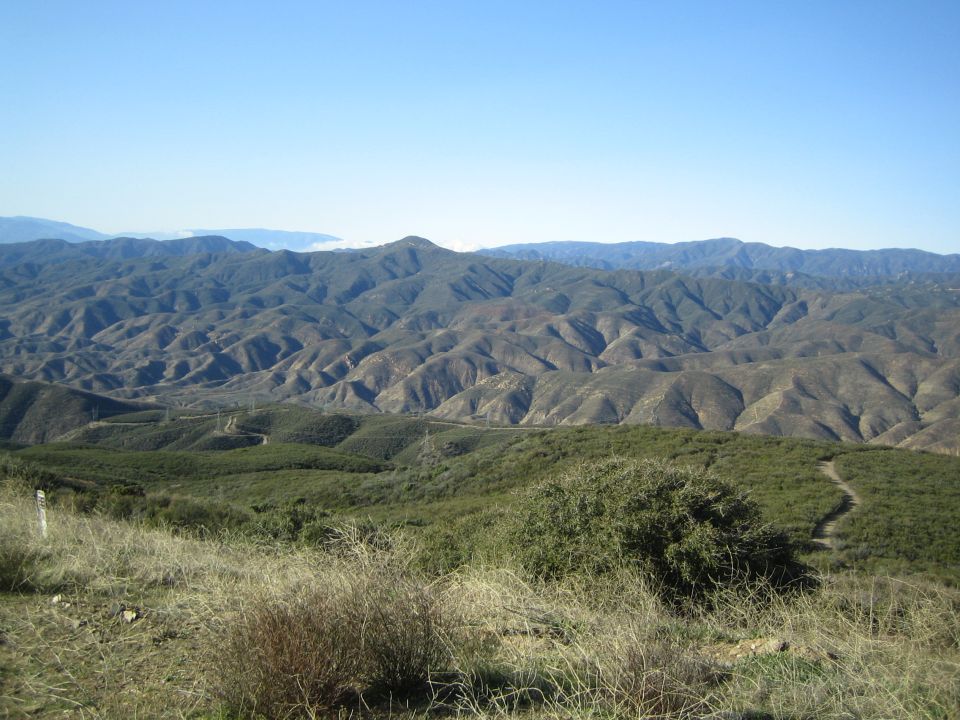 Eroded brown mountain ridges with green foreground hills under blue sky