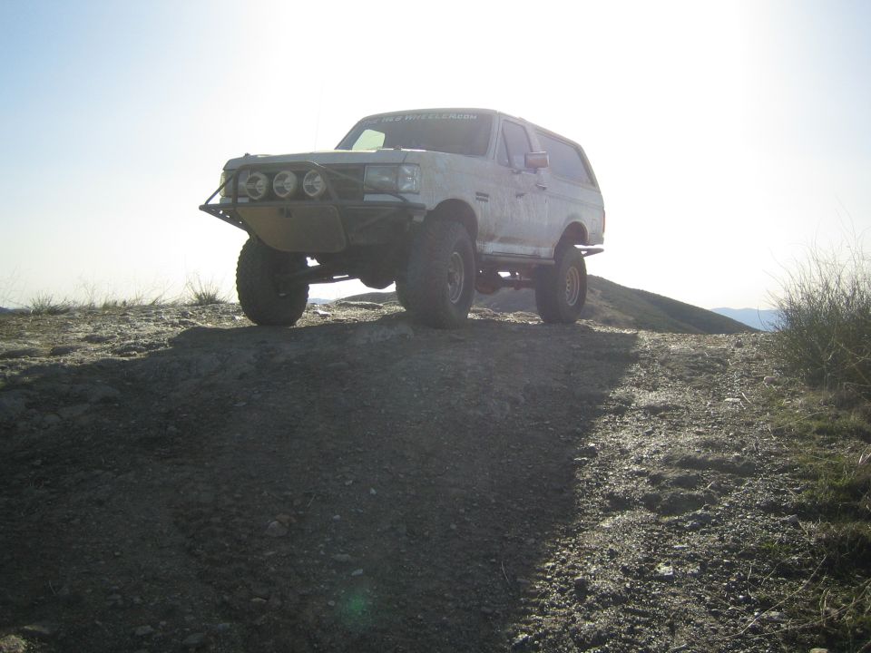 White lifted Ford SUV with tube bumper backlit on a dirt ridge