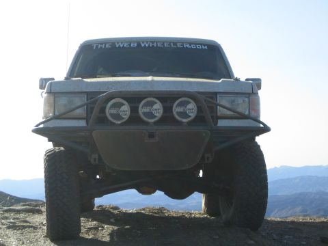 1990 Ford Bronco - Front view of a lifted off-road SUV with a tube bumper, three driving lights and a The Web Wheeler.com windshield decal.