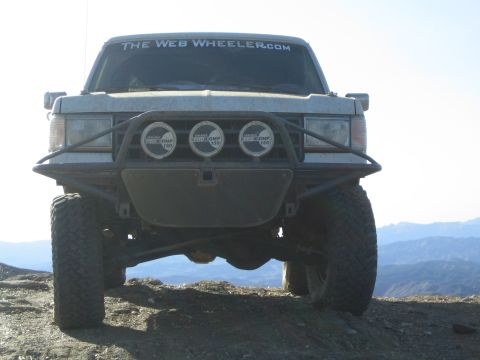 1990 Ford Bronco - lifted sport-utility vehicle sits on a rocky ridge, its front tube bumper holding three round off-road driving lights and a windshield bann…