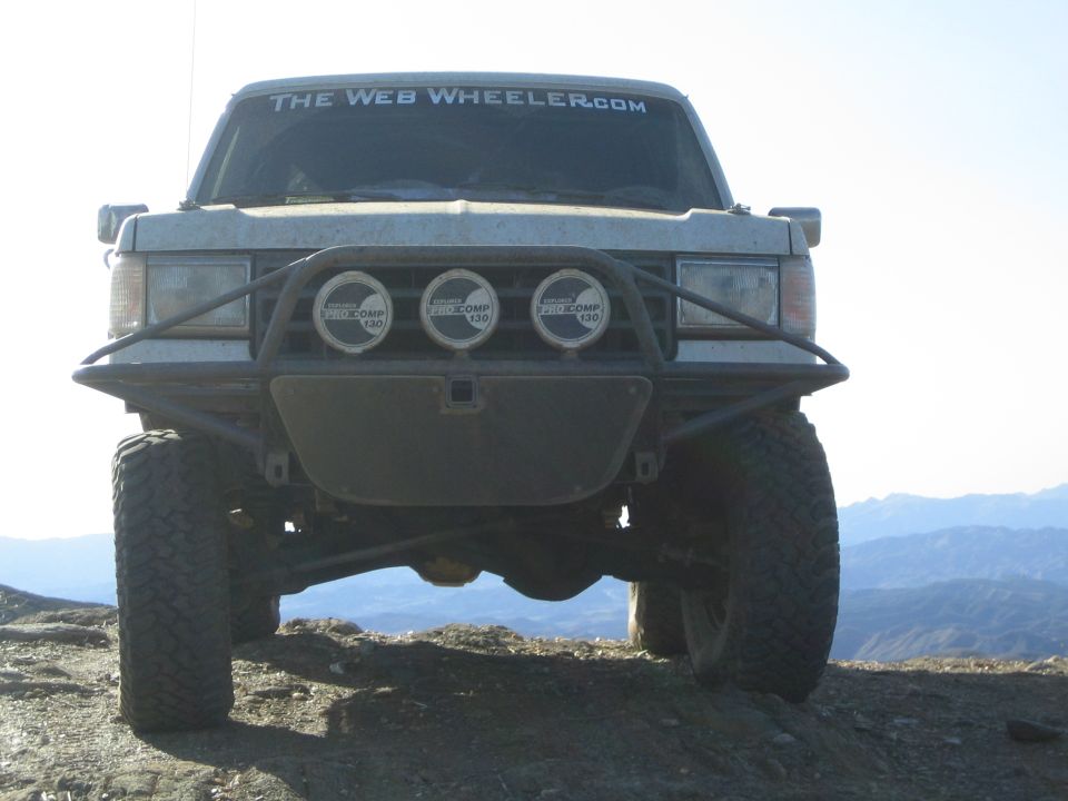Front view of lifted SUV on dirt ridge with off-road bumper and three round driving lights