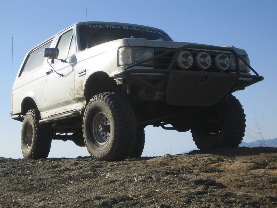 White lifted SUV with tube bumper and three driving lights on a dirt hilltop