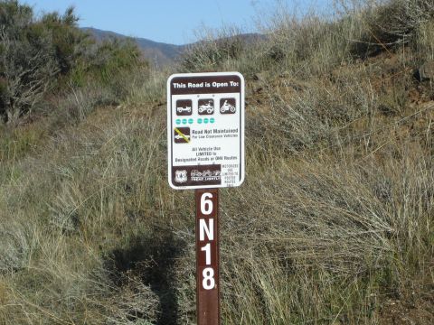 1990 Ford Bronco - brown Forest Service sign stating the road is open to jeeps, ATVs and motorcycles stands on a post marked 6N18 amid dry brush.