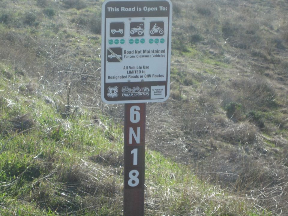 Brown Forest Service OHV sign on a post marked 6N18 against a grassy hillside