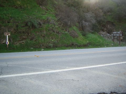 1990 Ford Bronco - two-lane paved road runs along the base of a green brushy hillside dotted with small brown directional road signs.