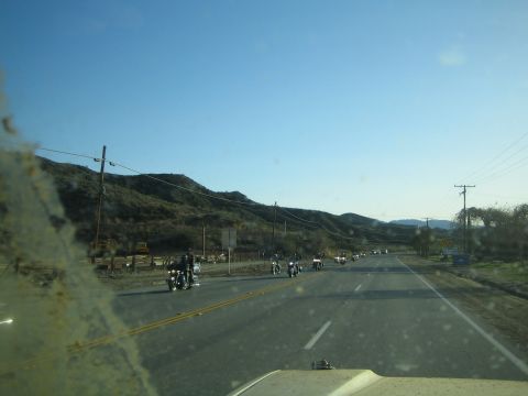 1990 Ford Bronco - Seen through a dusty windshield, a group of motorcycles travels along a rural two-lane highway flanked by dry hills.