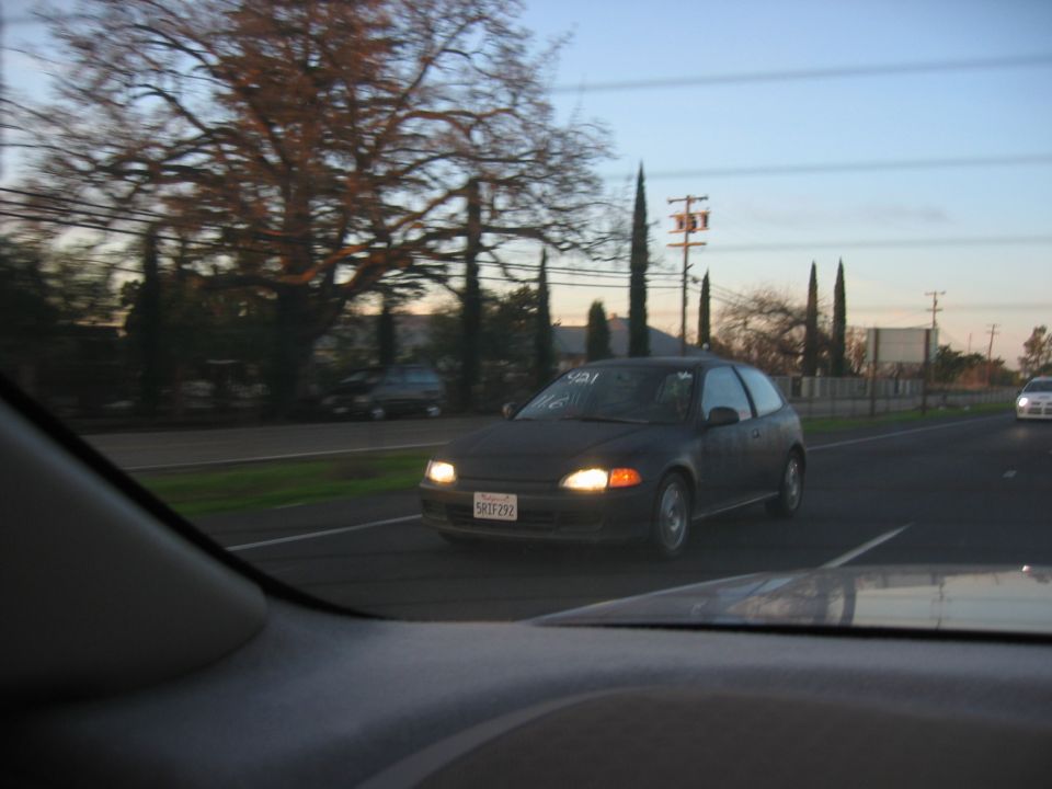 Dark gray hatchback with headlights on driving toward camera on a road at dusk, shot from inside another car