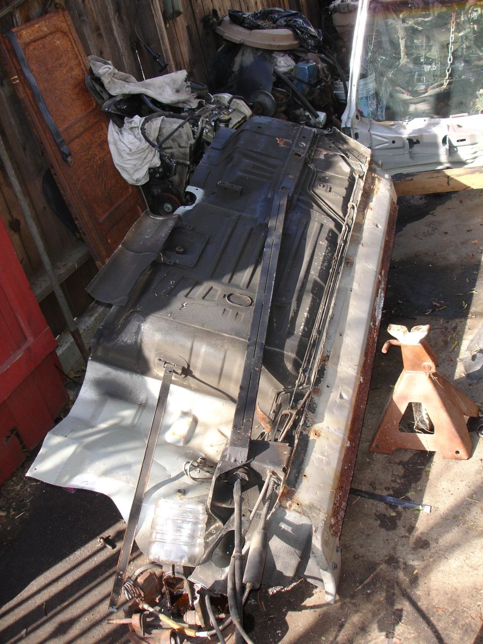 Cut-out car floor pan section on its side in a backyard, with lines attached and a rusty jack stand nearby