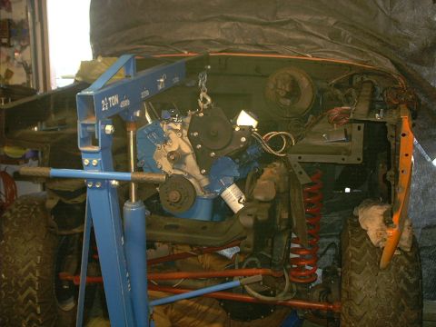 1978 Ford Bronco - An engine hoist is positioned to lift a blue engine out of an orange vehicle's engine bay.