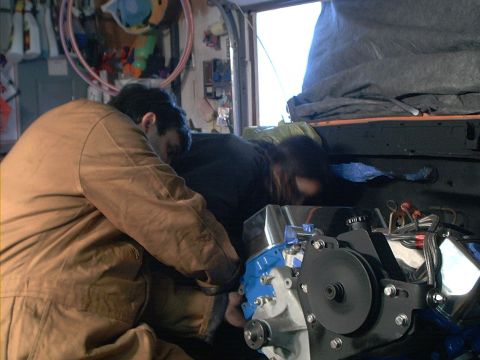 1978 Ford Bronco - Mechanics are installing a new engine into a vehicle in a garage setting.