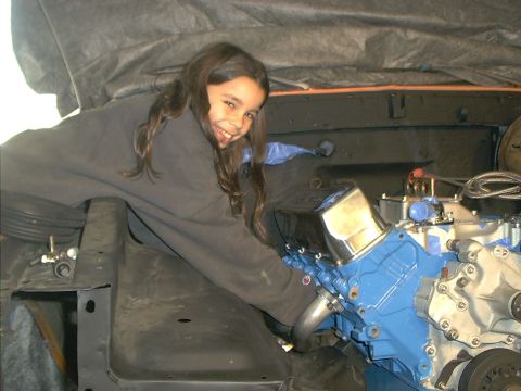1978 Ford Bronco - A young girl works on a blue engine, which is partially covered by a black tarp.