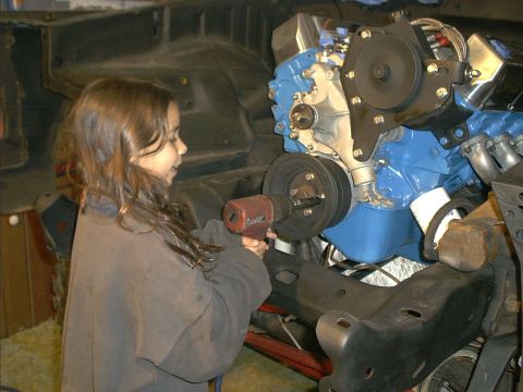 1978 Ford Bronco - A young girl works on a blue engine and chassis assembly with an impact wrench.