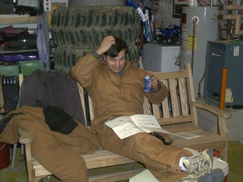 1978 Ford Bronco - A man relaxes in a garage setting, surrounded by various items including stacked tires and mechanical equipment.