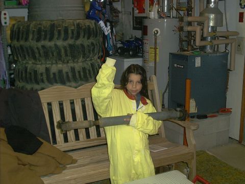 1978 Ford Bronco - A child dressed in a yellow jumpsuit holds a large metal pipe while standing in a garage setting.
