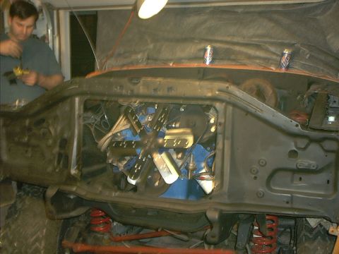 1978 Ford Bronco - The engine bay of a vehicle is visible, showing a blue engine block and a large fan. A person is working on the vehicle in the background.
