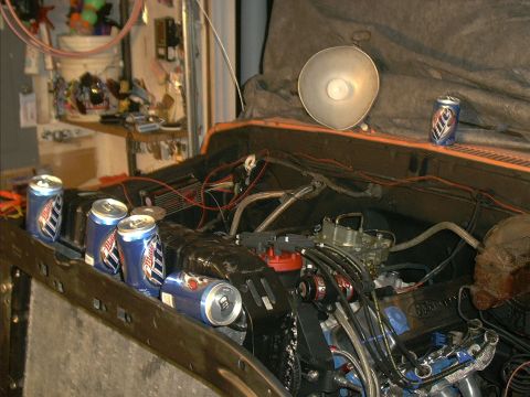 1978 Ford Bronco - Engine bay with beer cans on the fender and cowl. A light fixture hangs overhead.