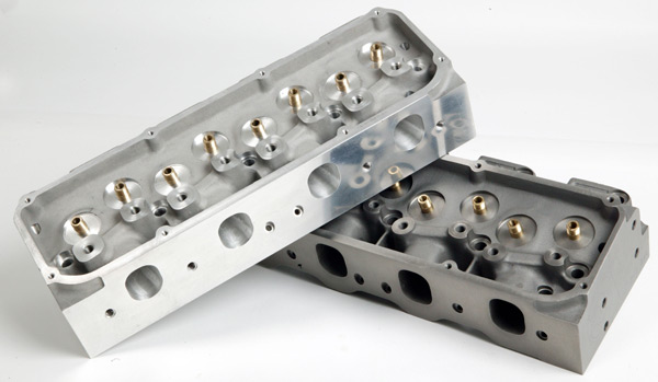 Two aluminum cylinder heads, one showing combustion chambers, the other intake ports, on white