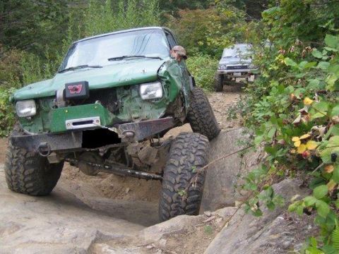 1990 Ford Bronco - Modified SUV with significant damage to the front end is attempting to climb over rocks.