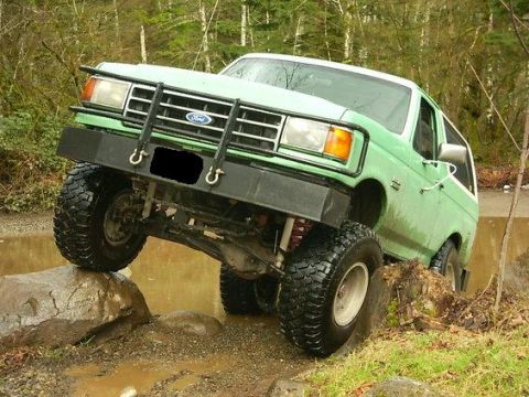 1990 Ford Bronco - This modified Ford Bronco is navigating a challenging off-road course with large tires and a raised suspension.