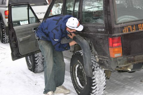 2003 Jeep TJ - A man works on the fender of a Jeep Cherokee XJ parked in the snow next to a Ford pickup.