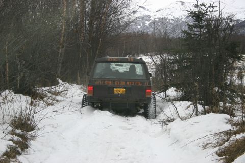 2003 Jeep TJ - A Jeep Cherokee XJ navigates a snow-covered trail, with text on its rear window humorously suggesting it might flip over.