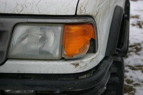 2003 Jeep TJ - Front corner of a white vehicle with a damaged turn signal lens and visible mud and snow.